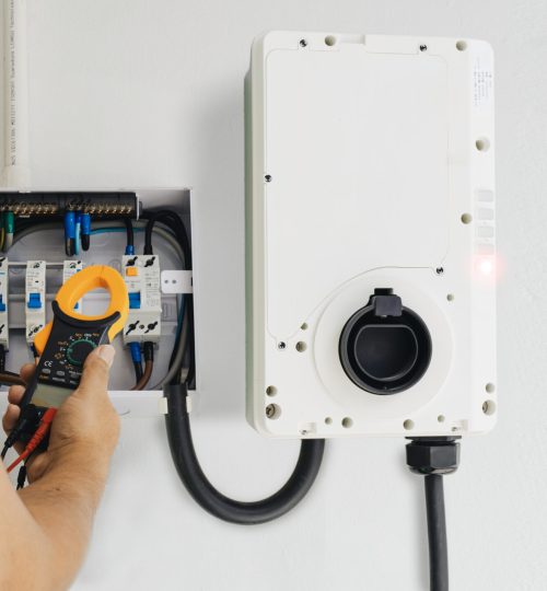 Close-up of an electrician performing tests with a clamp meter during home EV charger installation. Focusing on precision and safety for reliable electric vehicle charging.