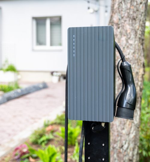Close-up view of electric vehicle charger mounted outdoors in home driveway. Setup reflects commitment to clean energy and convenient personal charging